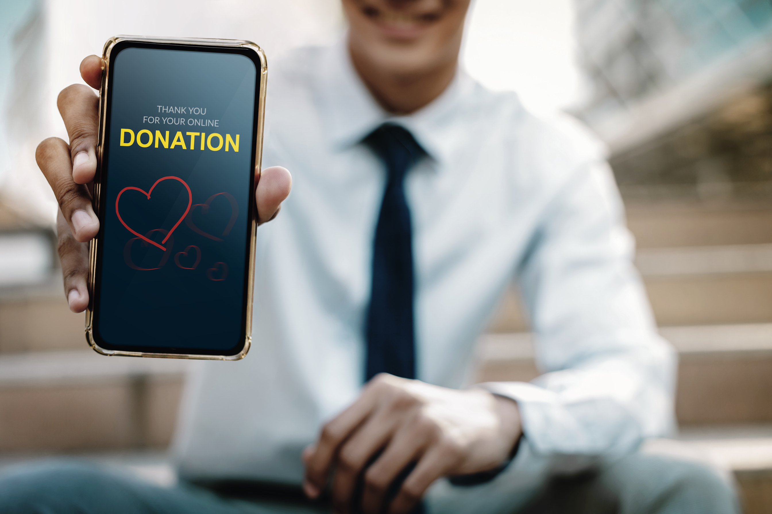 Online Donation Concept. Smiling Businessman showing a Donate Message on Mobile Screen